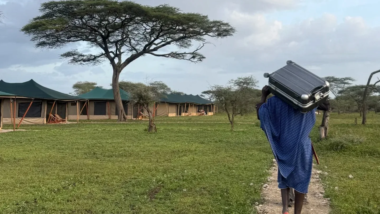 Camp staff member carrying luggage toward tented safari accommodation in Tanzania