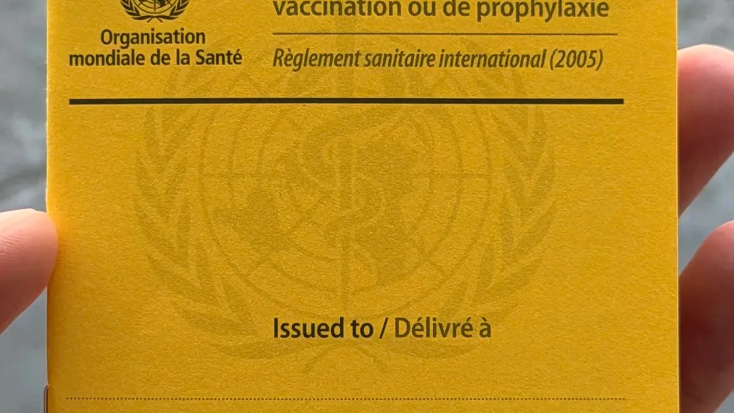 Yellow international certificate of vaccination or prophylaxis held in one hand