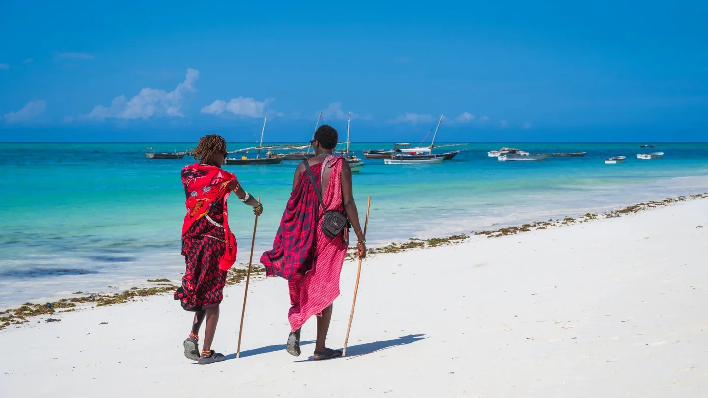 Two people in red garments walking along a white-sand beach in Zanzibar